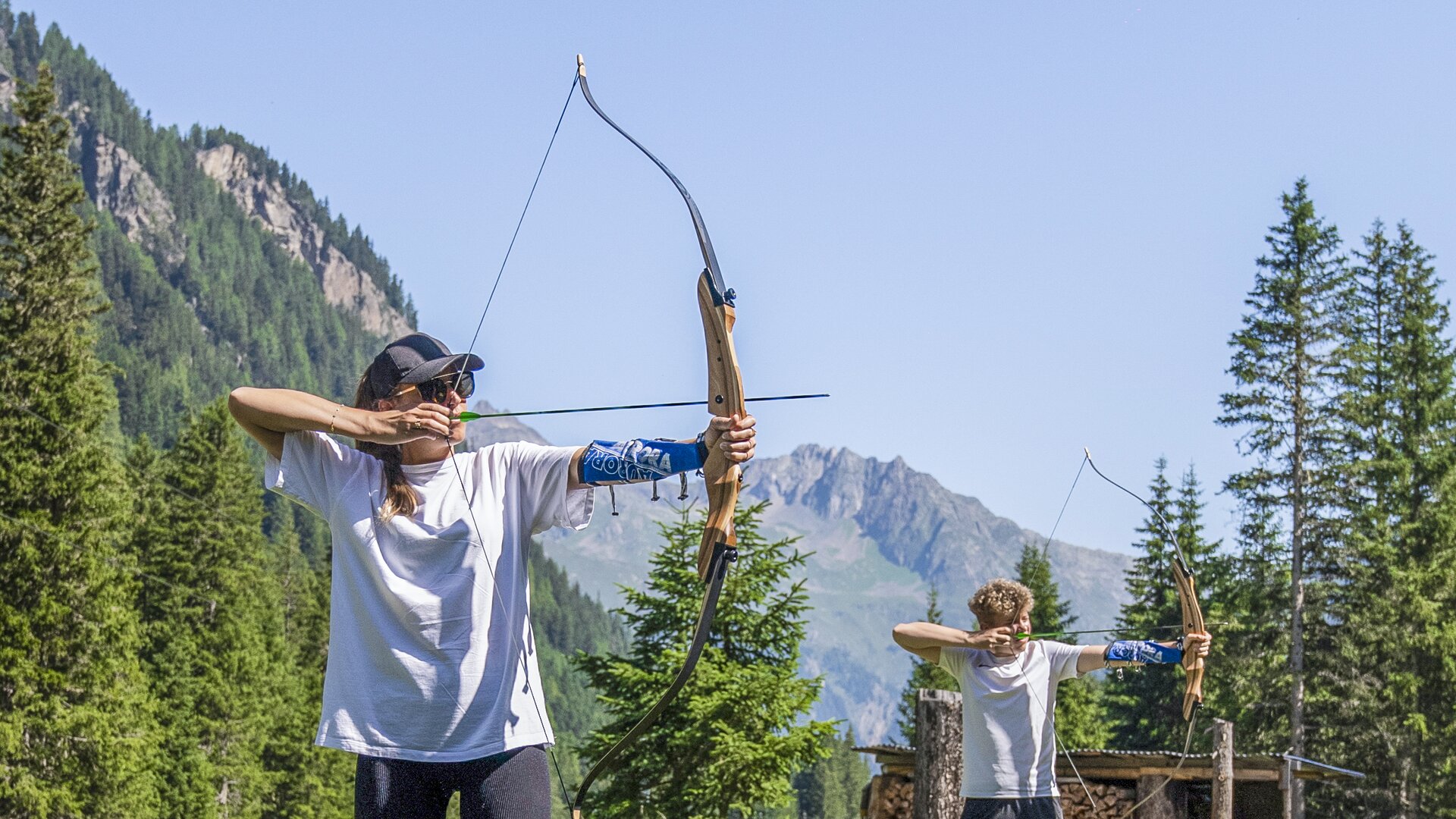 Eine Frau und ein Mann zielen beim Bogenschießen im sommerlichen Ischgl konzentriert in die Ferne.