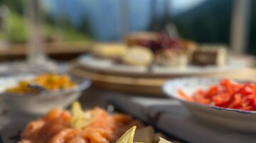 Ein lecker angerichtetes Fischgericht mit Zitrone und verschiedenen Beilagen. Im Hintergrund sind Berge und ein klarer Himmel sichtbar.