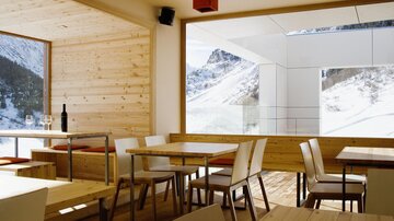 A modern restaurant with wood-paneled walls and large windows. The view of the snow-covered mountains creates a cozy atmosphere.