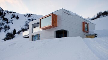 A modern building in a snow-covered landscape. The surroundings feature mountains and clear skies.