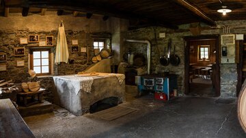 A rustic room with stones and wood, showcasing traditional craftsmanship. Tools and old photographs can be seen on the walls.
