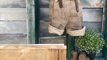 A sweet, wooden wall with a pair of hanging short leather pants and fluffy flowers. Below is a wooden sign with the inscription "Almstubn".