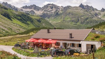 A cozy cabin in the mountains with red sun umbrellas. The surroundings are green and mountainous, ideal for nature lovers.