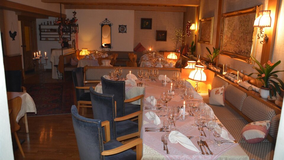 A cozy restaurant with a long, covered table and warm light. The decor is inviting and friendly.