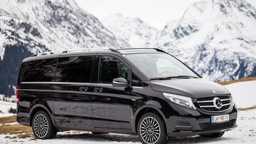 A black van is standing on snow-covered ground with mountains in the background. The landscape is wintry and picturesque.