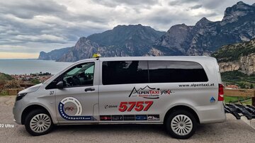 A taxi is standing in a picturesque landscape with mountains and water in the background. The sky is cloudy and the surroundings are calm.