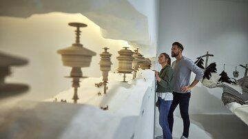 A couple stands in front of an art installation with sculptural objects on a bright wall. The atmosphere is modern and inspiring. | © TVB Paznaun - Ischgl