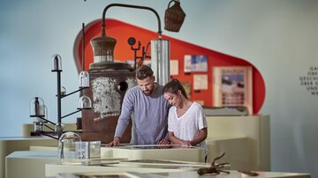 A couple is looking at exhibits in a museum. In the background, historical objects and informative panels can be seen. | © TVB Paznaun - Ischgl