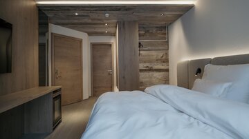 A modern bedroom with a large bed and a wooden design. The walls are light and the lighting creates a cozy atmosphere.