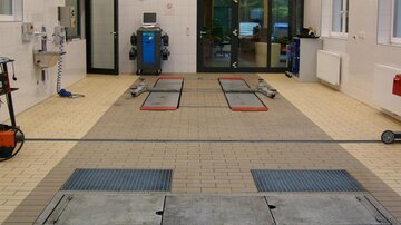 A modern car wash facility with an open area and several washing stations. The floor is paved, and there are various devices for vehicle cleaning.