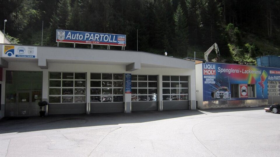 A workshop called Auto Partoll with large garage doors. In the background, there are trees and a colorful advertising board.