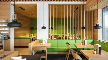 A modern restaurant with wooden elements and a green wall. The tables are made of wood and the lighting is stylish.