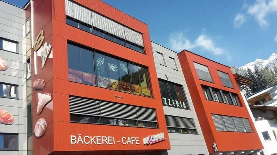 A modern building with a striking red facade. On the ground floor, there is a bakery and a café.
