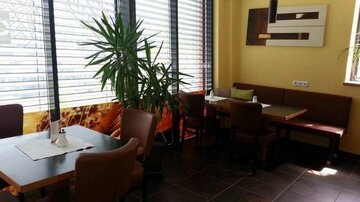 A modern restaurant with a cozy atmosphere. Large windows let in plenty of light, and plants create a pleasant ambiance.