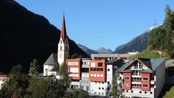 A picturesque village with a church and modern buildings. In the background, mountain landscapes can be seen.