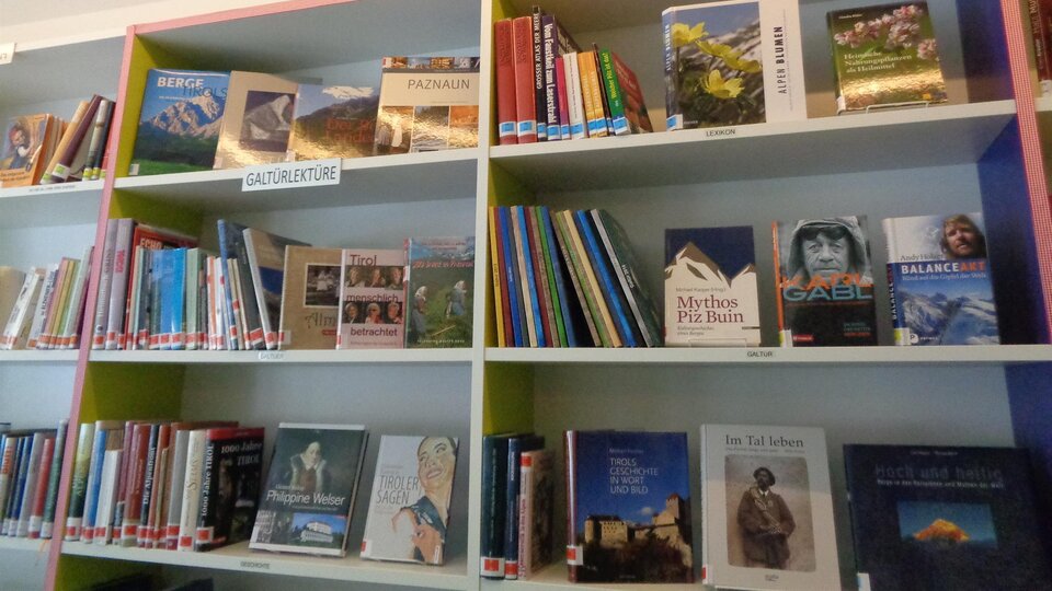 A bookshelf with many different titles that displays the word "TIROL" above it. The books cover various topics and genres.