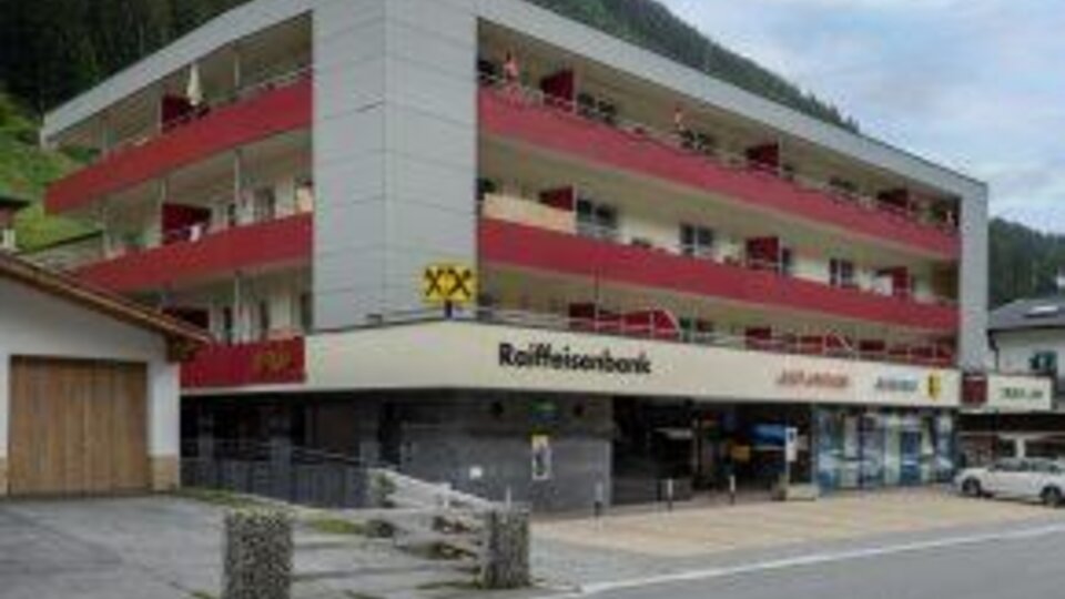 A modern building with several floors and balconies.  
At the bottom, there is a Raiffeisen bank and shops.