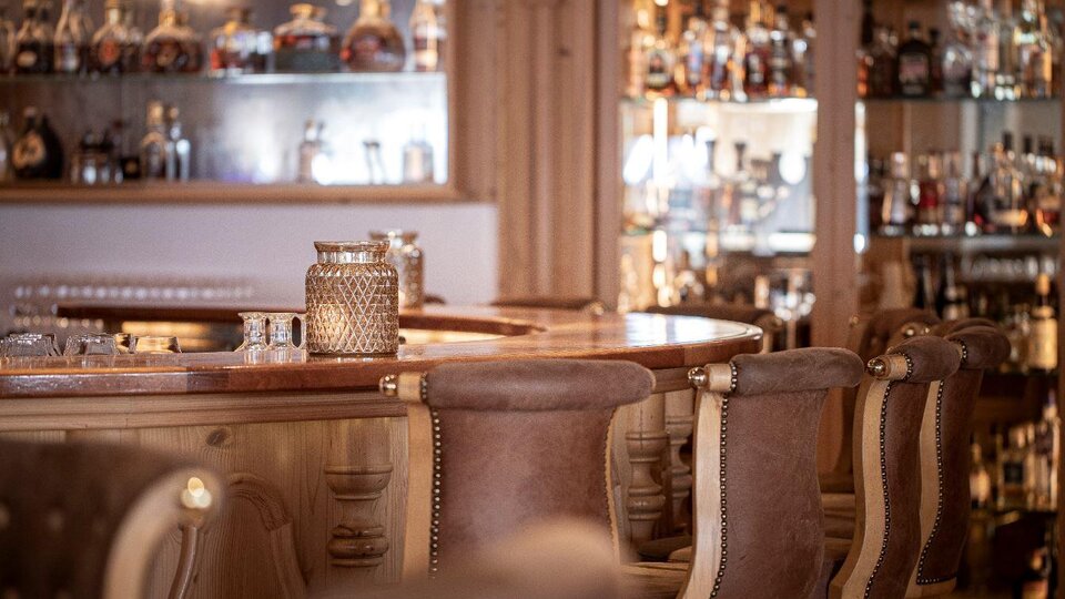 A stylish bar with wooden-clad chairs and elegant glasses. In the background, shelves with various spirits are visible.