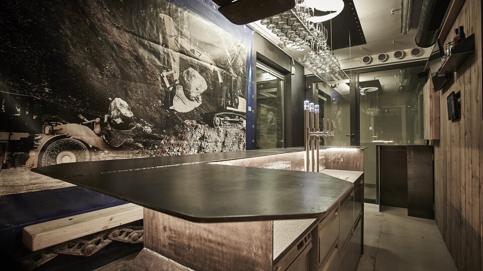 A modern interior with a generous bar counter and rustic wooden elements. On the wall hangs a large black-and-white image depicting a mining scene.