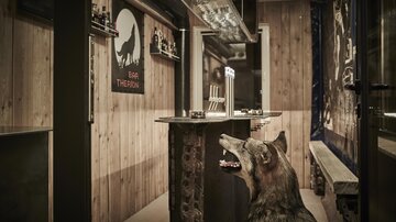 An inviting bar area with wooden walls and a counter. A wolf head decor and cozy atmosphere create a unique ambiance.
