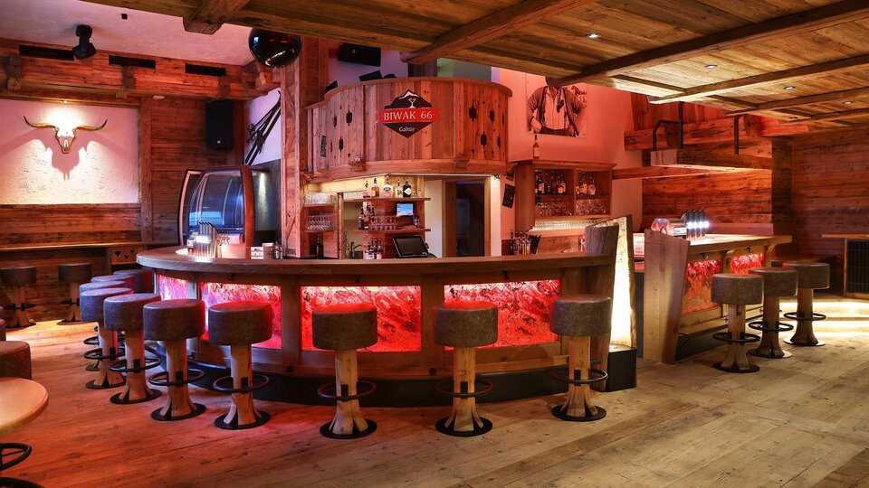 A cozy bar with wooden paneling and round stools. The lighting creates an inviting atmosphere.