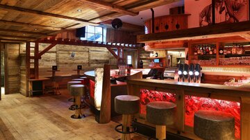 A cozy bar with wooden decor and warm lighting. The counter is well stocked and there are bar stools for seating.