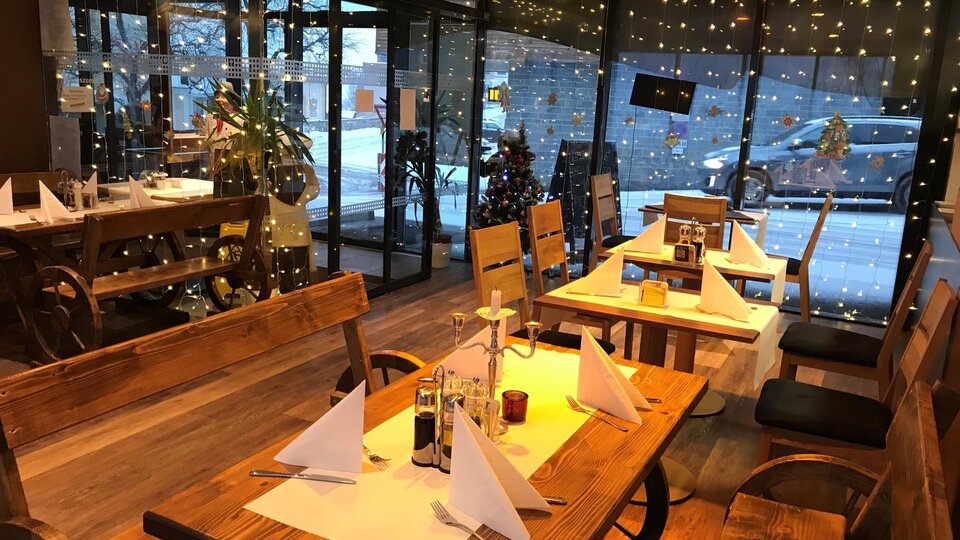 A cozy restaurant with wooden tables and chairs. Large windows reveal Christmas decorations and atmospheric lighting.