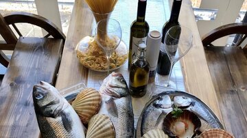 A table with fresh fish, shellfish, and scampi, surrounded by spaghetti and olive oil. The arrangement is appetizing and showcases various seafood.