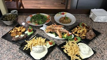 A festive meal on a table with various dishes. There are fries, fried chicken, salad, and sauces.