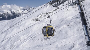 A cable car glides over a snow-covered landscape. In the background, majestic mountains are visible.