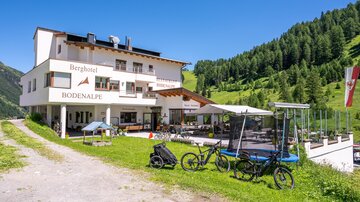 Ein modernes Berghotel mit schöner Fassadengestaltung. Vor dem Hotel stehen Fahrräder und der grüne Bergwald erstreckt sich im Hintergrund.