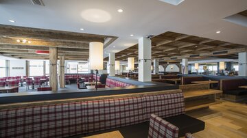 A modern restaurant with a wooden ceiling and cozy seating areas. The decor is bright and inviting, ideal for a pleasant atmosphere.