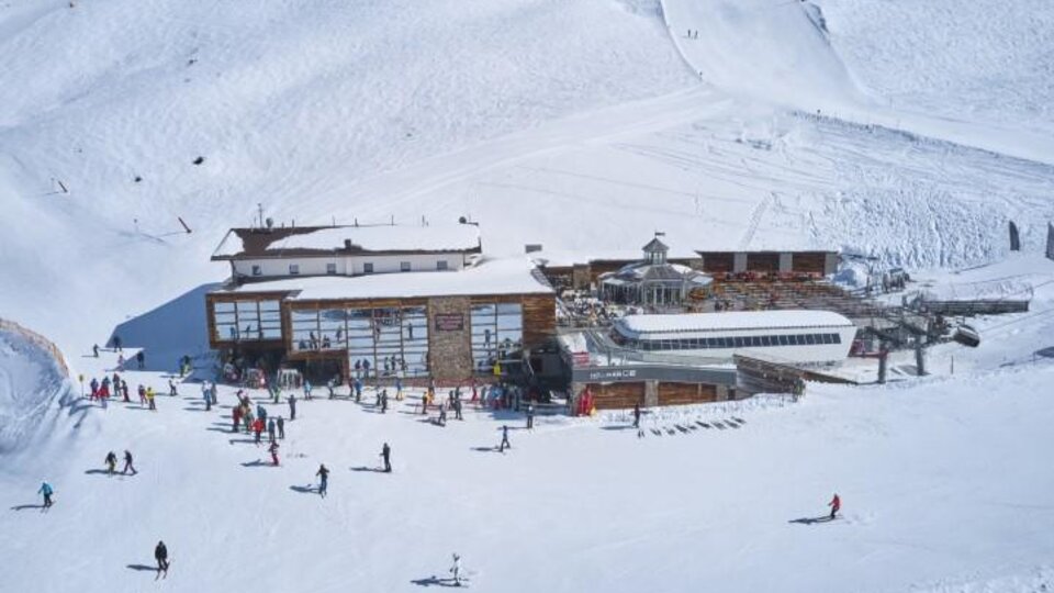 A ski resort with plenty of snow and a large wooden building. Numerous skiers and snowboarders enjoy the wintry landscape.