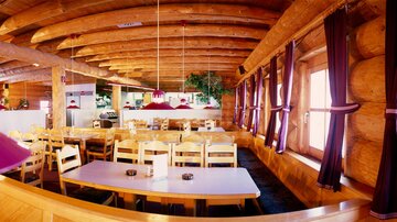 A cozy restaurant with a wooden ceiling and many tables. The decor has a warm, inviting atmosphere.