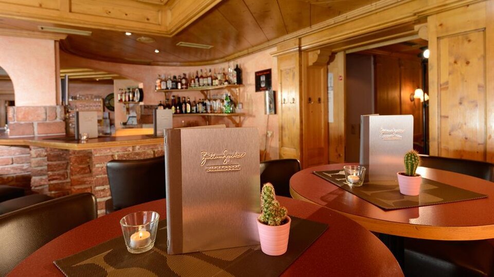 Ein gemütliches Restaurant mit Holzwänden und einer einladenden Bar. Auf den Tischen stehen Menükarten und kleine Pflanzen in Töpfen.