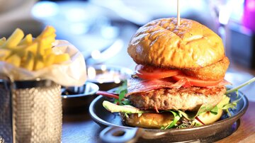 Ein köstlicher Burger mit frischen Tomaten und Salat auf einem Teller. Daneben liegt eine Portion Pommes frites.