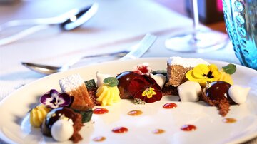 Ein kunstvoll angerichteter Dessertteller mit verschiedenen Süßspeisen, essbaren Blumen und bunten Saucen. Die Präsentation ist elegant und ansprechend.
