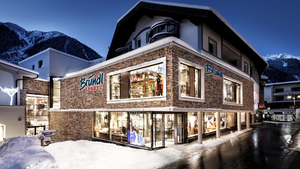 Ein modernes Geschäftshaus mit großen Fenstern in den Alpen. Es ist mit Schnee umgeben und die Beleuchtung sorgt für eine gemütliche Atmosphäre bei Nacht.