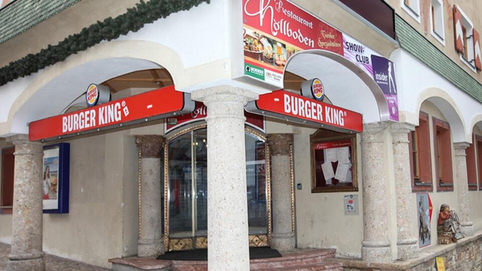 A Burger King restaurant with a striking red sign. The building has columns and is in an urban environment.