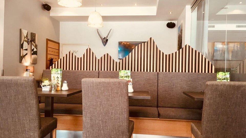A modern restaurant with cozy seating areas and a decorative mountain-themed wall. The light is bright and friendly, creating an inviting atmosphere.