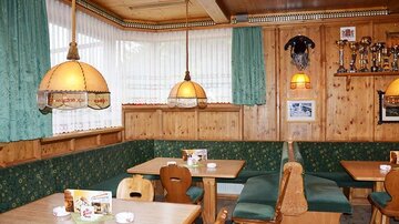 A cozy guest room with wood-paneled walls and green curtains. The tables are made of wood and equipped with inviting benches.