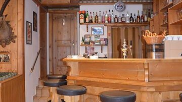 A cozy bar with a wooden counter and stools. In the background, shelves with drinks and glasses can be seen.