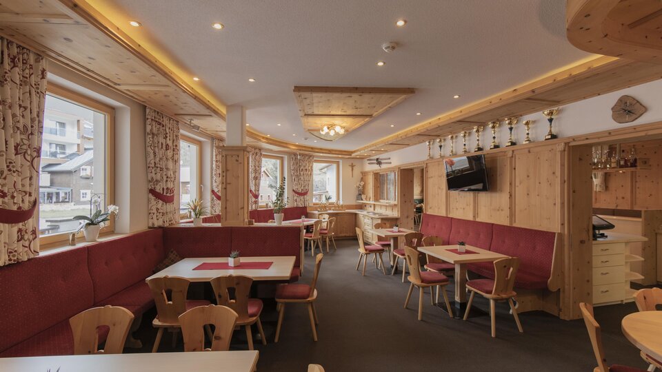 A cozy restaurant with wood decor and red upholstered benches. There are tables with space for guests and large windows that let in natural light.