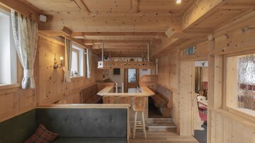 A cozy room with wood paneling and large windows. There is a long table and a bench that look inviting.