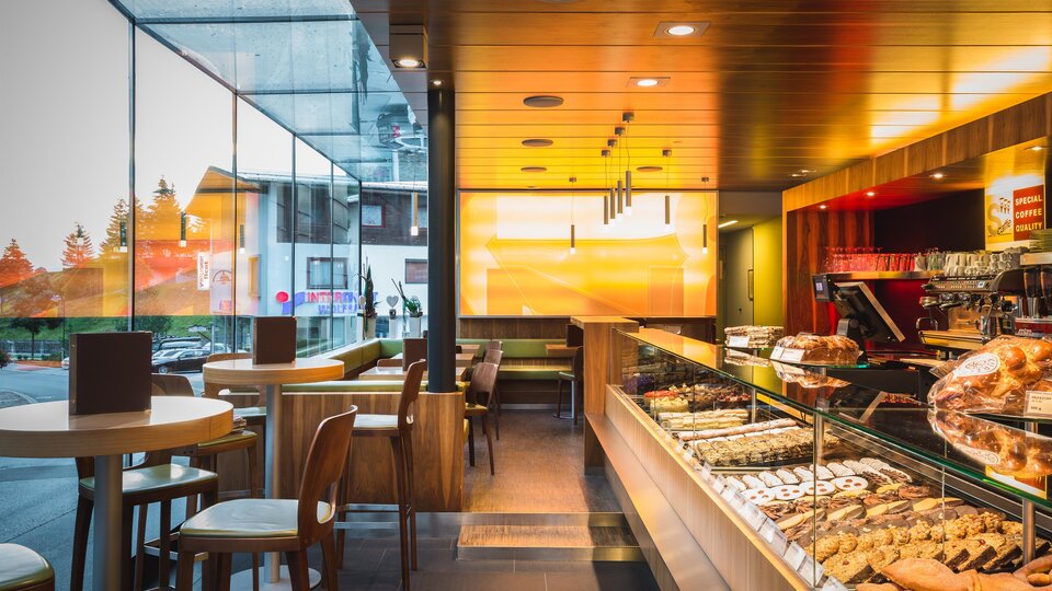 A modern café with a large display full of cakes and pastries. Bright colors and plenty of natural light create an inviting atmosphere.
