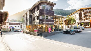 A modern building with large windows and an inviting entrance. In the background, mountains and a picturesque street view can be seen.