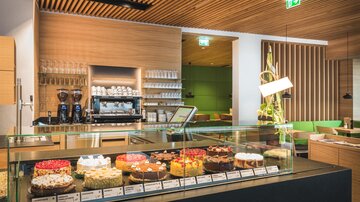 A modern café with a selection of colorful cakes and an elegant, bright interior. The display case showcases various cakes that invite you to linger.