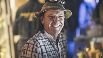 A smiling man with a hat and a checkered blouse. In the background, blurred light sources can be seen.