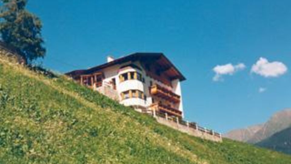 A beautiful house on a hill, surrounded by green meadows. The sky is blue with a few clouds.