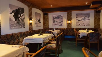 A cozy restaurant with wooden furniture and tables covered with white tablecloths. Impressive black-and-white photos of mountain landscapes hang on the walls.